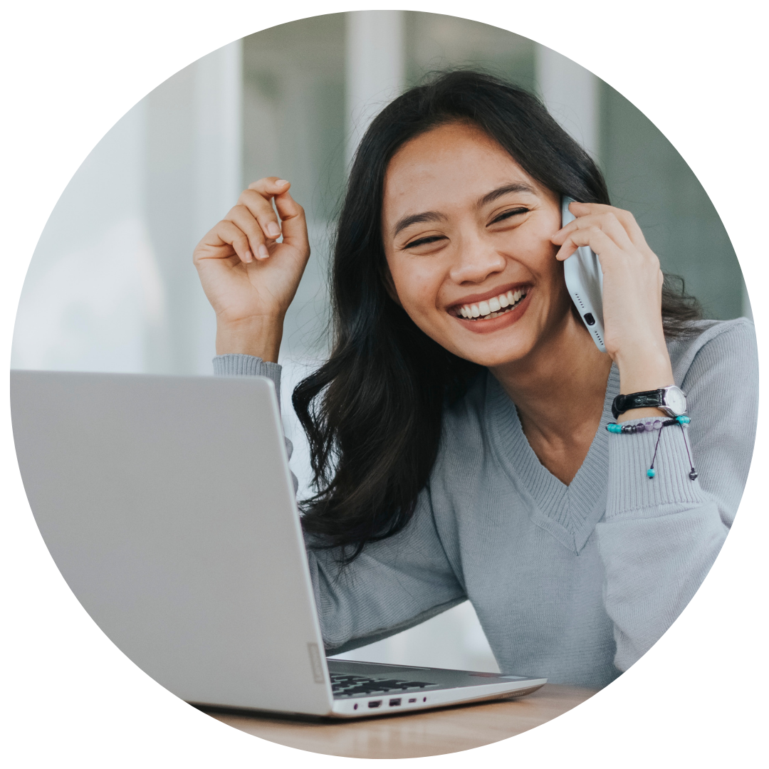 Woman on phone smiling sitting at desk with laptop open.