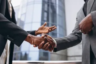 A man and woman in business attire shaking hands outside a corporate building, representing a formal agreement or collaboration.