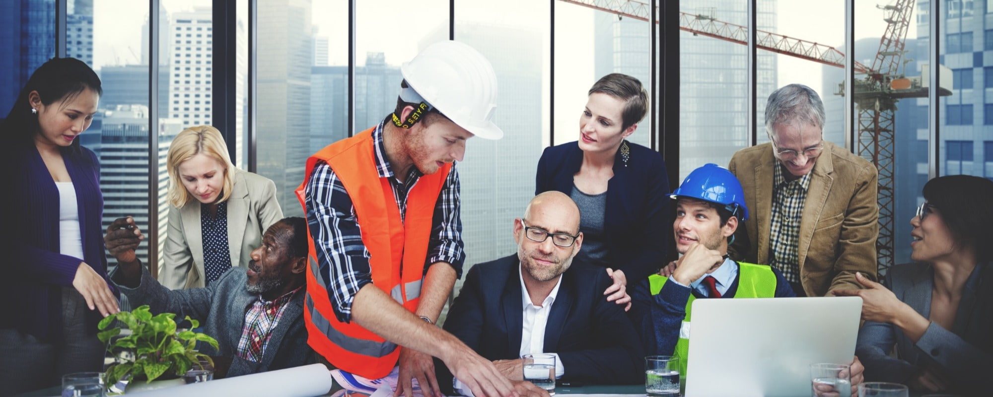 man with Hi-vis jacket on with hard hat and delivery driver, plant manager, administrator having an interview around a table with crane inbackgroud in city 