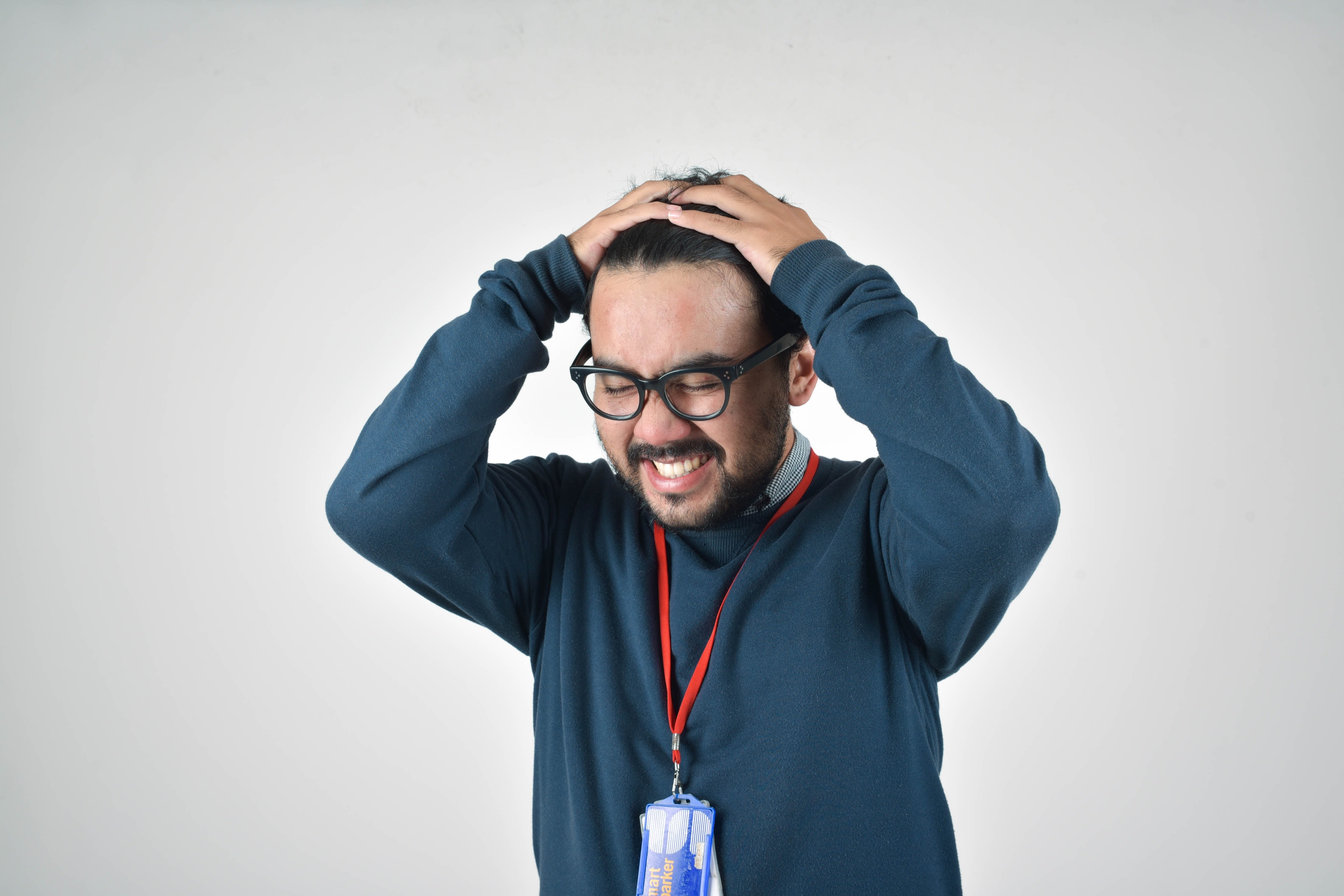 A man in glasses and a blue shirt holds his head, appearing deep in thought or stressed.