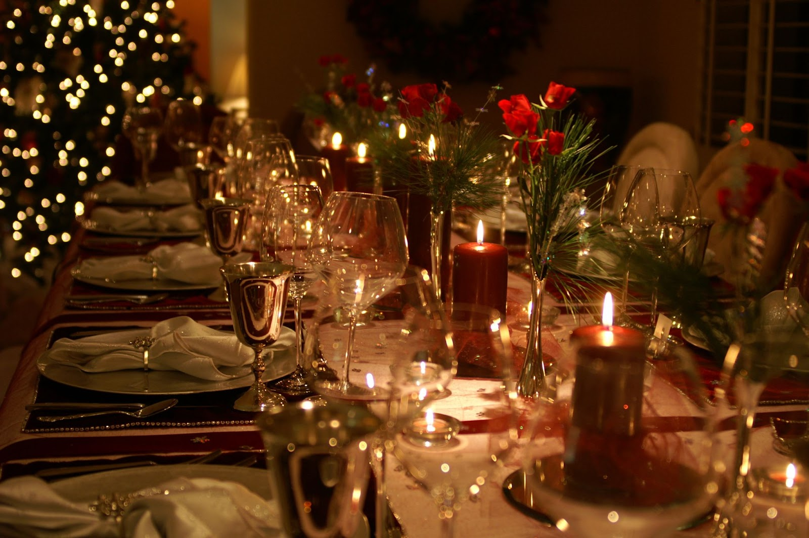 Christmas dinner spread with red candles and flowers in the centre of ornate table.