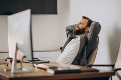 A man with a beard at his desk, appearing relaxed and too comfortable during work hours.