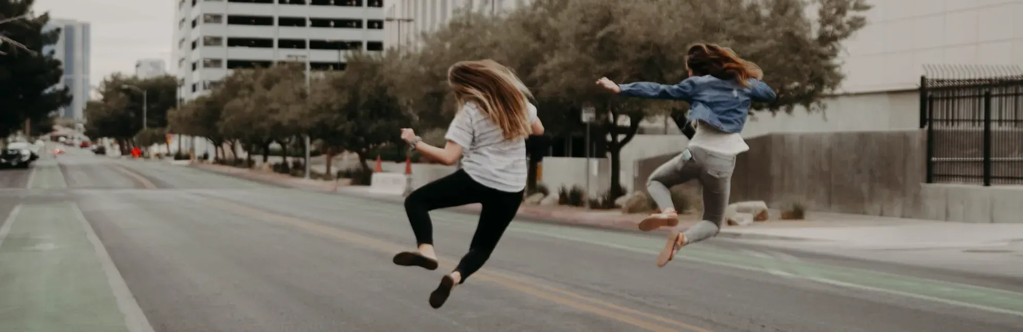 Two women joyfully jumping in the air on a city street, celebrating their successful job-sharing arrangement.