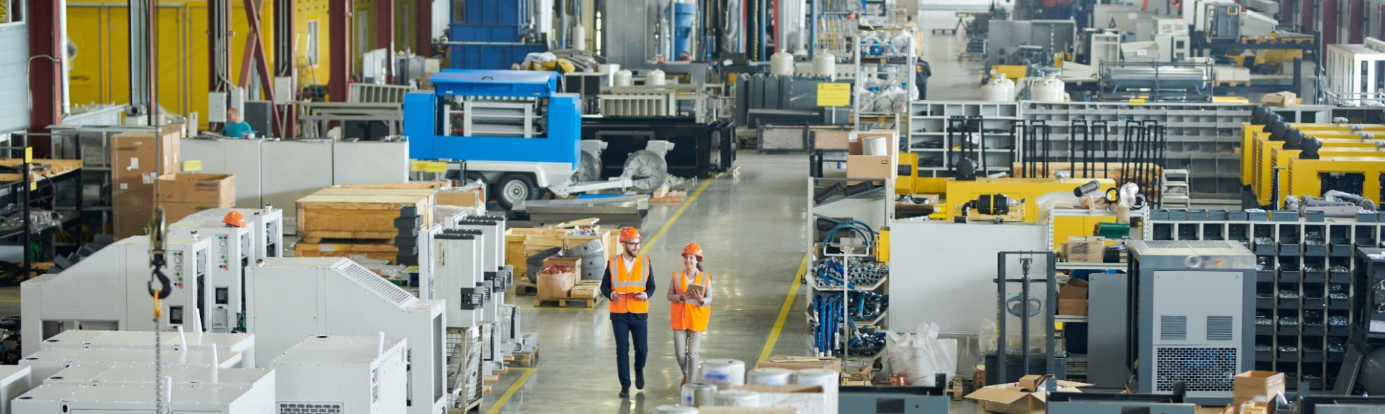 Operators in manufacturing setting, man and woman in high vis and hard hats carrying clip board