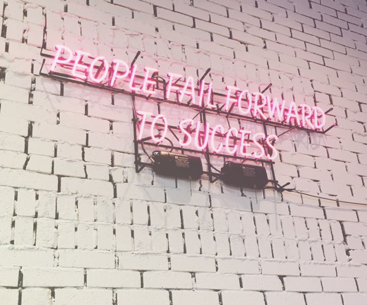 white brick wall with pink neon sign saying people fail forward to success