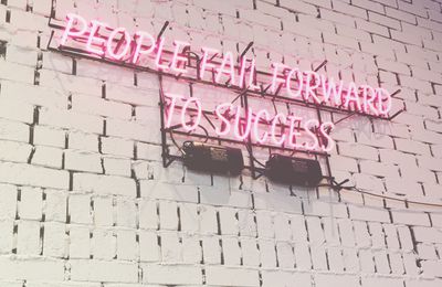 white brick wall with pink neon sign saying people fail forward to success