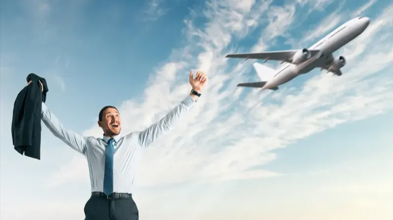 a cheering man in a suit outside with a blue sky and an airplane flying by.