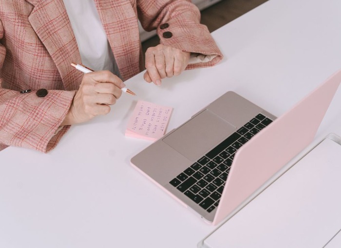 Woman in pink suit writing to-do list on pink post-it