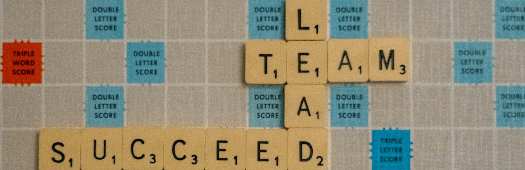 A Scrabble board featuring the phrases "team, lead, succeed" representing key principles in effective leadership.