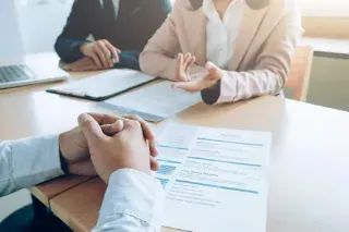 A man and woman sit at a table, reviewing a resume together, engaged in a discussion about job opportunities.