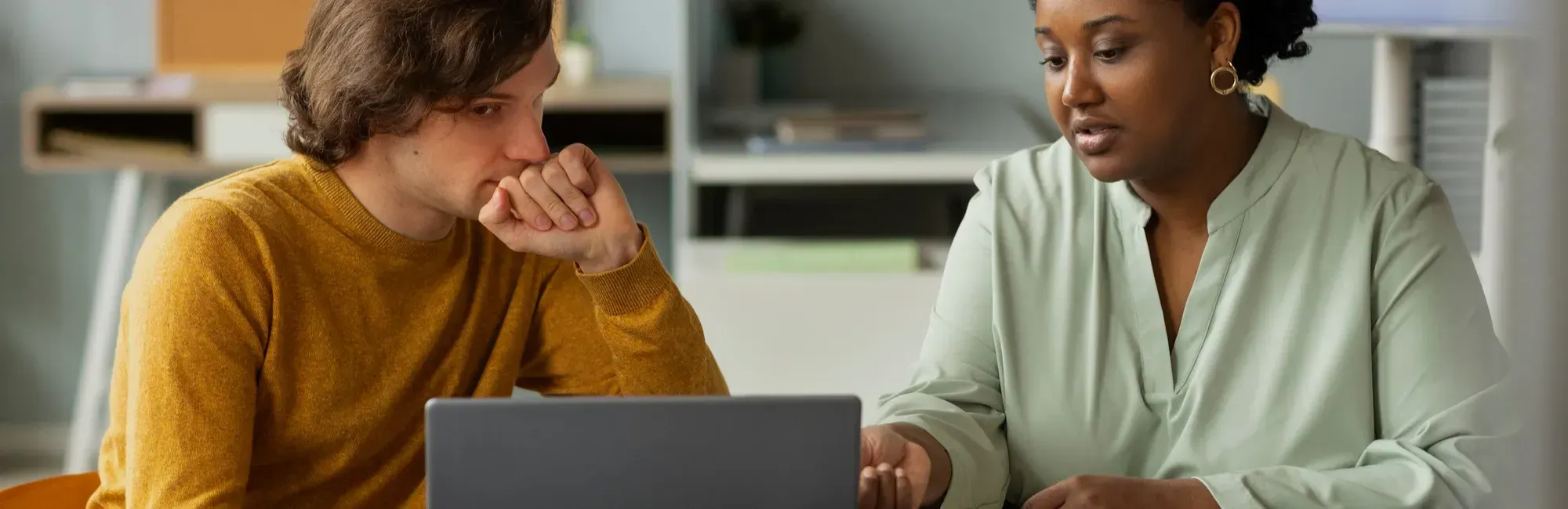 A man and woman seated at a table, collaborating on a laptop in a mentor-mentee setting.