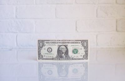 one dollar bill on white surface in front of white brick wall