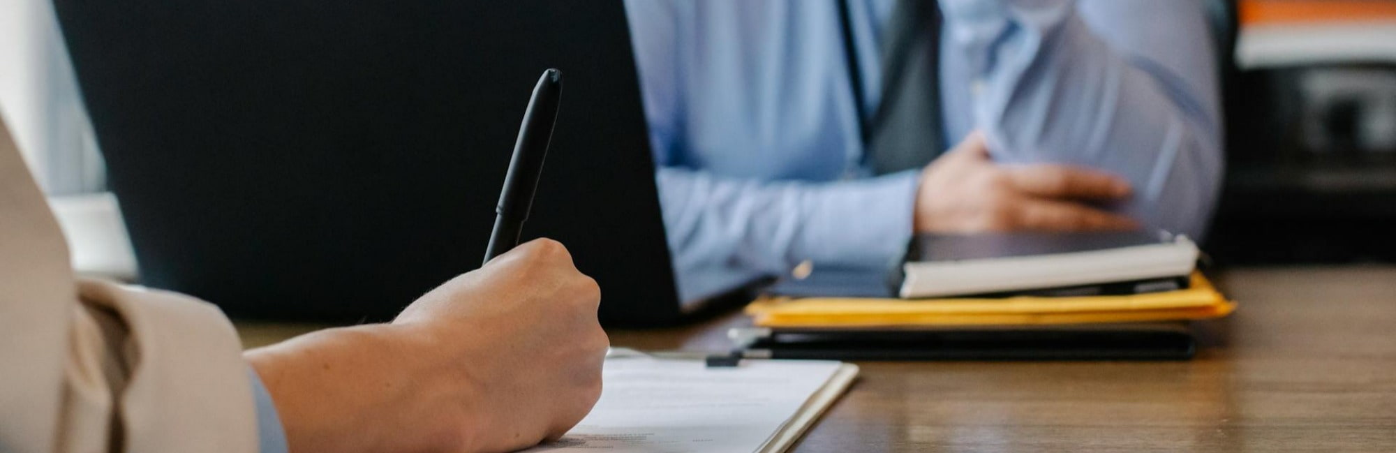 A man and woman sit at a desk; the man is interviewing for an accounting position using a laptop.