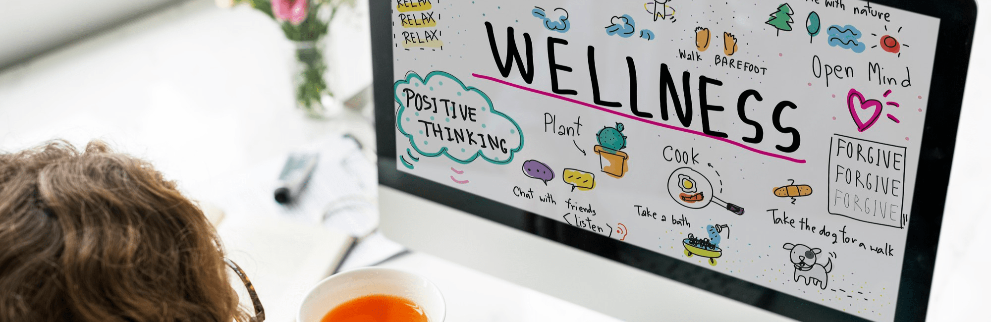Woman holding a cup of tea, focused on a computer screen displaying wellness resources for workplace wellbeing.