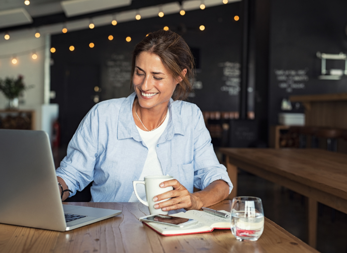 woman happily working on a laptop in a cafe with coffee and fairy lights