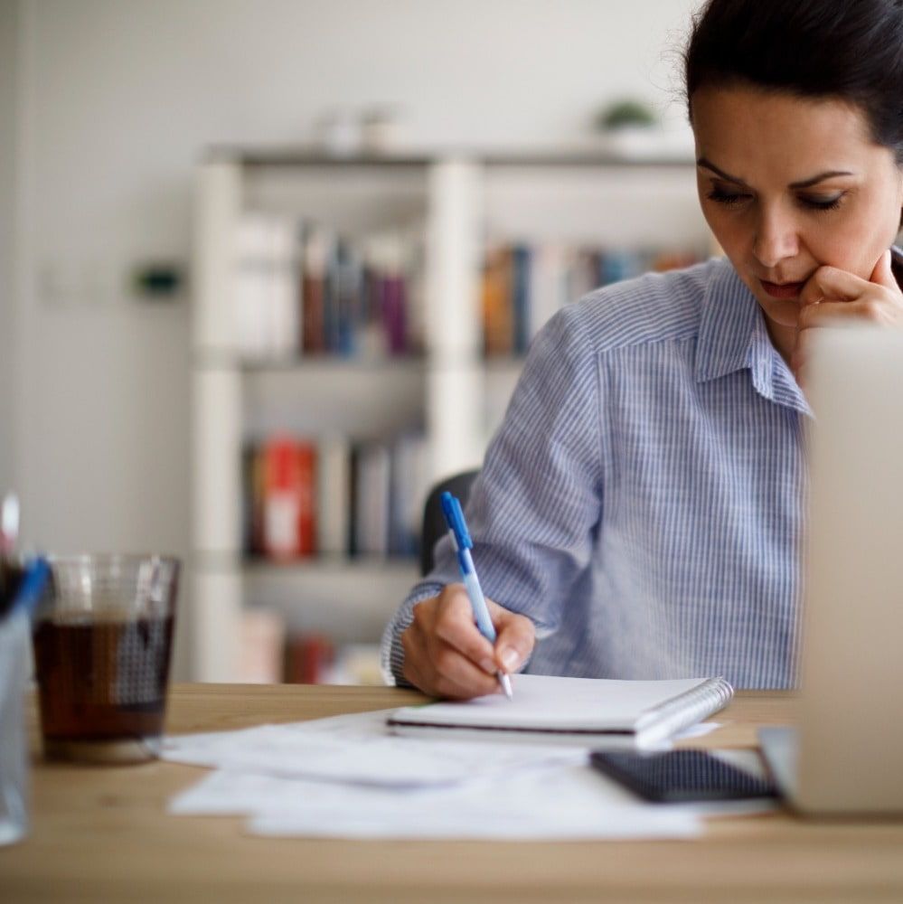 woman sitting at desk holding pen writing in notepad prepping for job interview