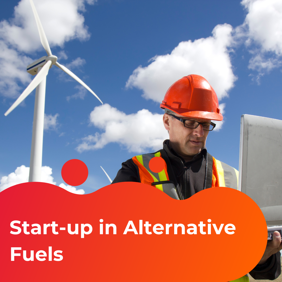 Start-up in Alternative Fuels Case Study. Image shows a man in a yellow and orange high vis and orange hard hat looking at a computer. Behind him is the sky and a windmill.