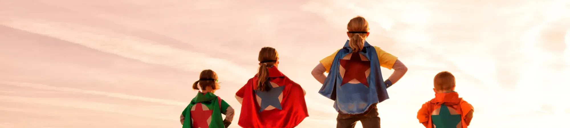 vier kinderen op een rijtje als superhelden. Ze hebben allemaal een cape om met verschillende kleuren en een ster. 