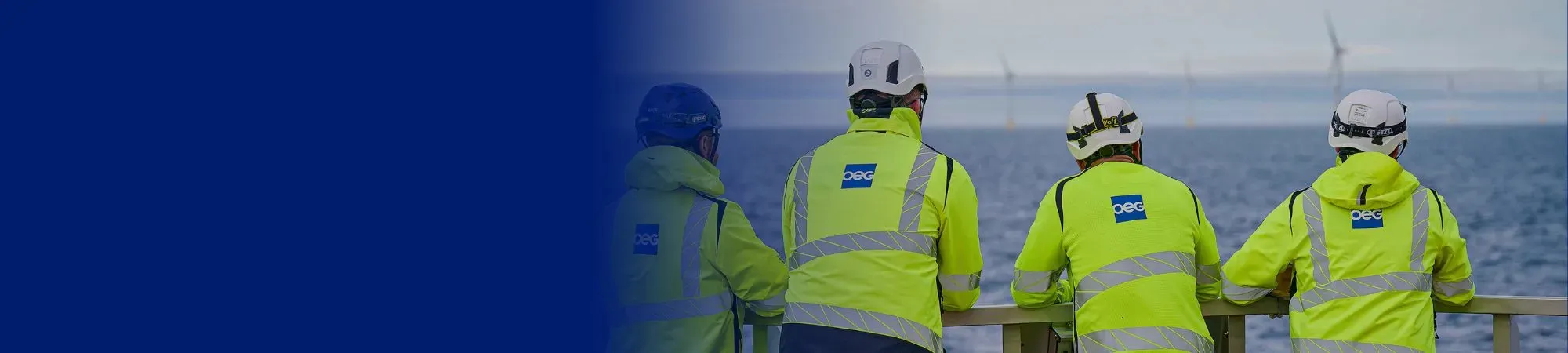 Four offshore workers looking out to an offshore wind farm.
