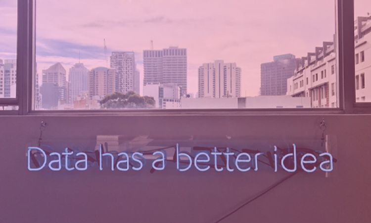 window with city view and neon sign on wall below saying data has a better idea