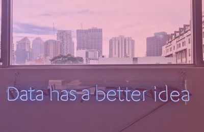 window with city view and neon sign on wall below saying data has a better idea
