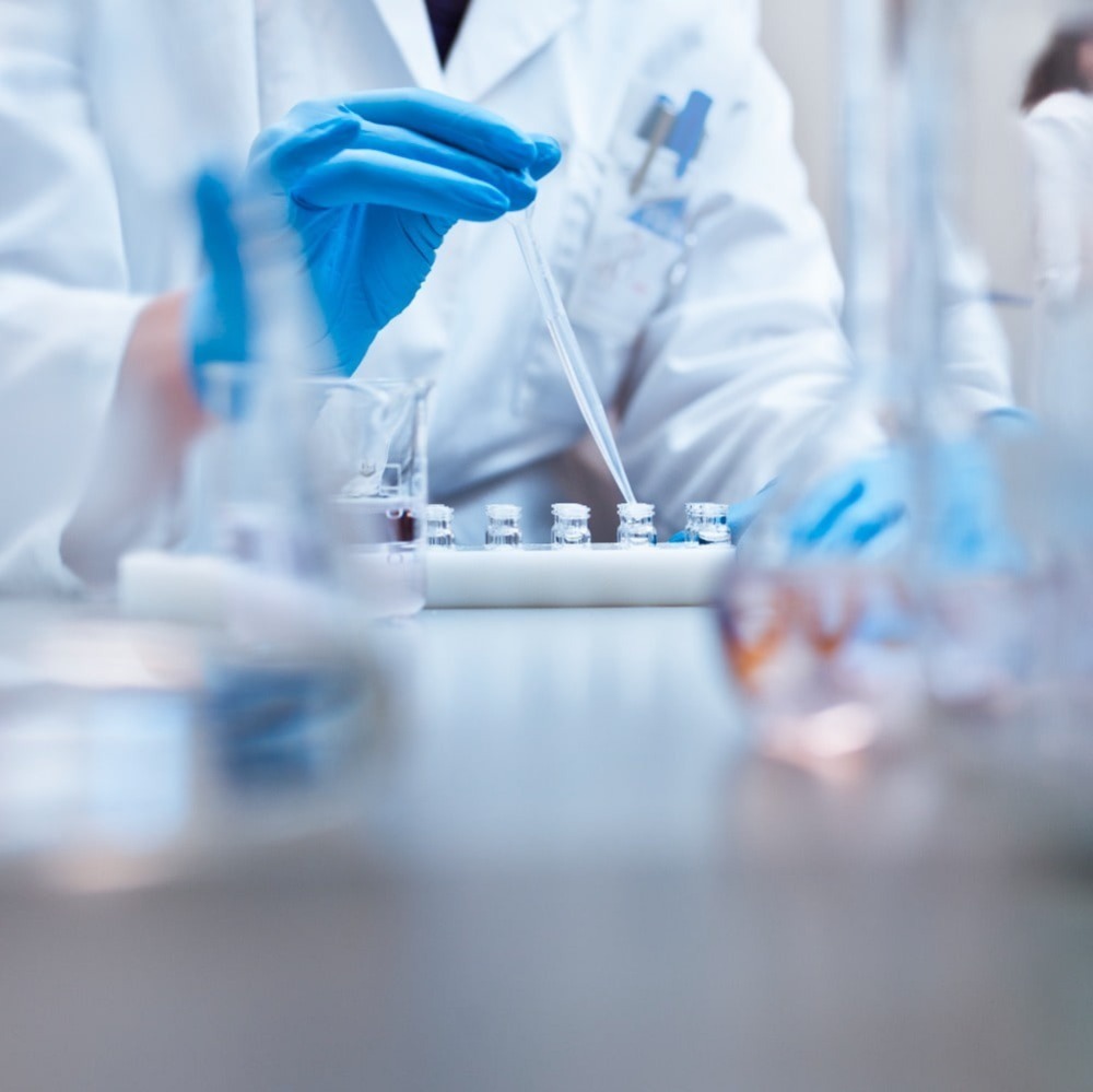 Scientist filling vials with solution through pipette in test tube rack in a science lab