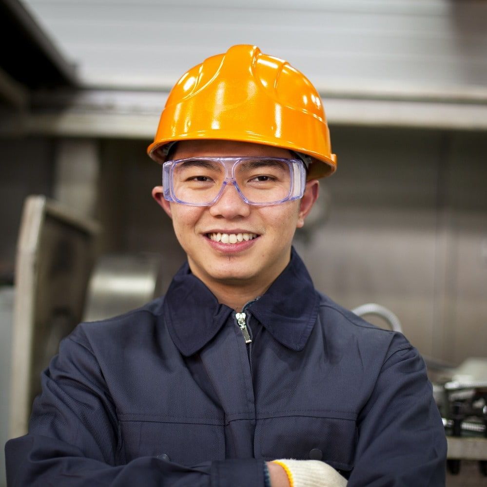 Image of a man wearing a yellow hard hat and safety glasses, smiling