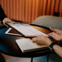 A woman holds a clipboard with her Transactional Finance CV on it while a man reviews the CV.