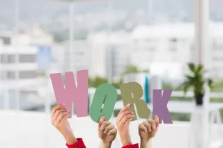 Hands holding colorful cut-out letters that spell the word "work" against a neutral background.