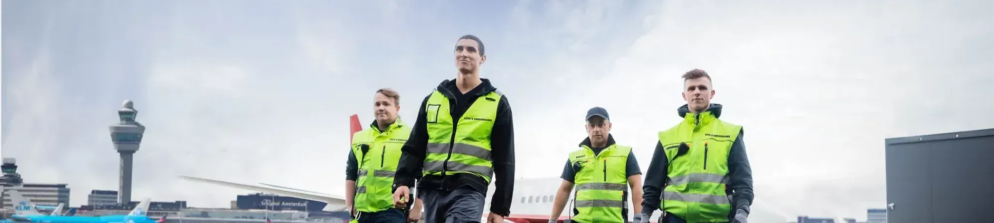 vier werkende mannen op het platform bij Schiphol met gele hesjes aan