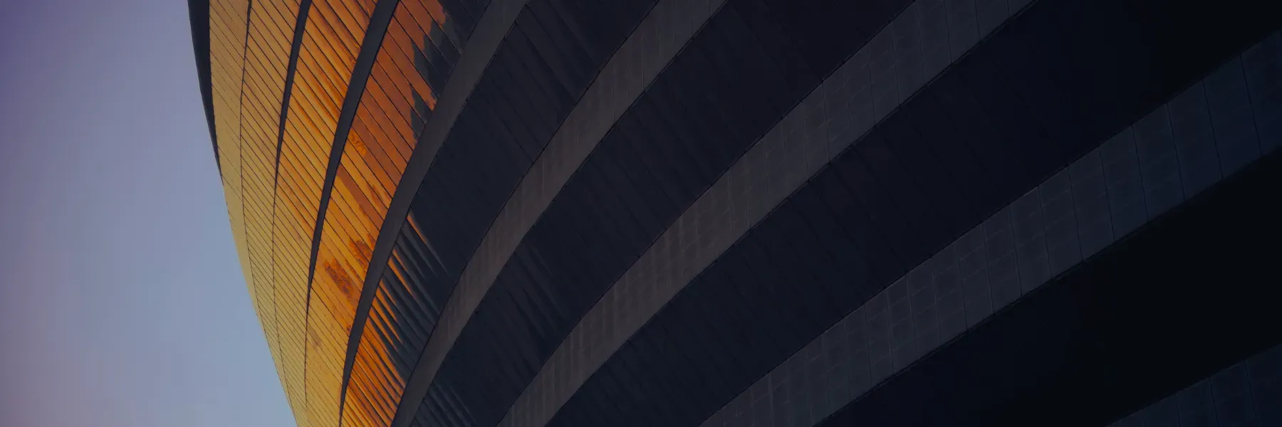 A large dark building with an orange glow reflecting in the windows