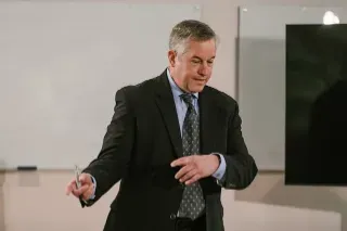 A suited man delivers a presentation, showcasing his leadership skills to an engaged audience.