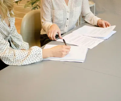 Two women engaged in signing papers at a table, demonstrating collaboration.
