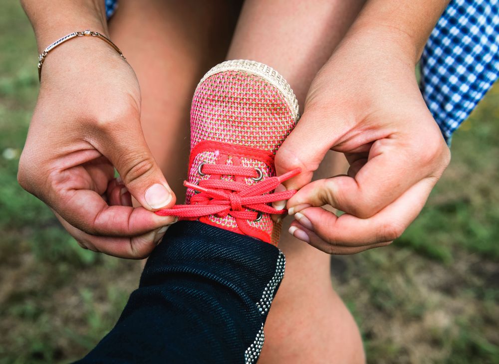 Close up of mother's hands tying toddler's red shoelaces