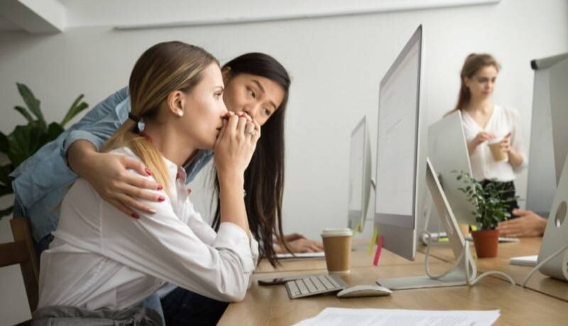 Professional woman consoling woman looking upset at computer screen 