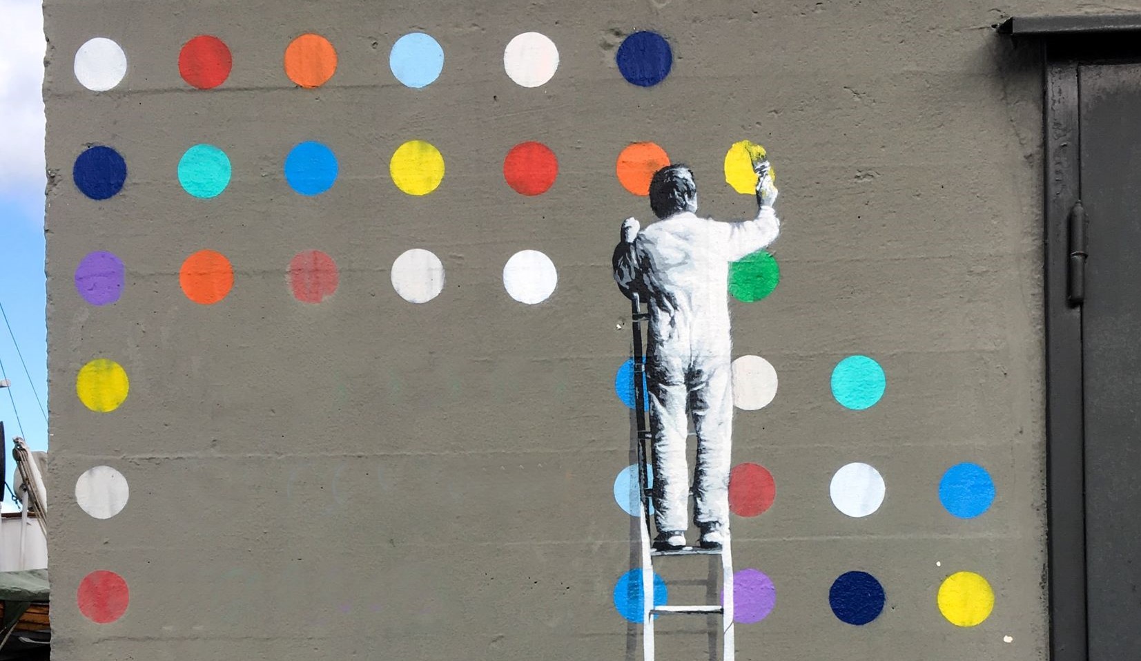 Man painting coloured circles disrupting the plain grey wall