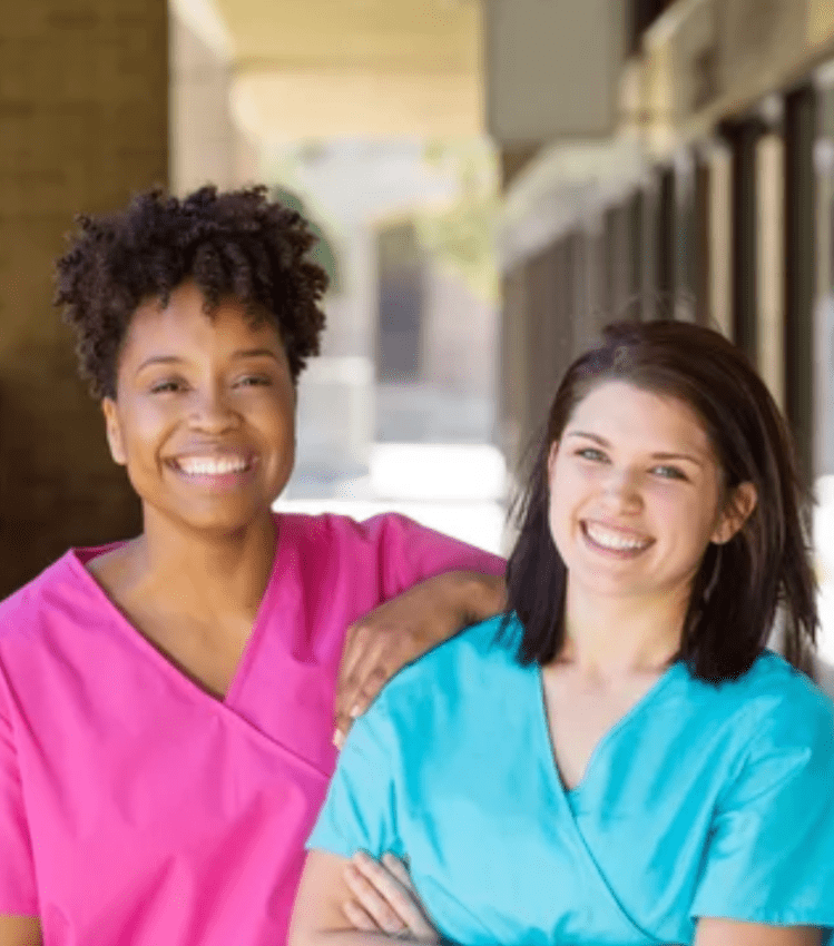 Two nurses smiling, standing up with their arms crossed