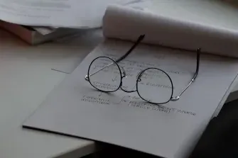 A pair of glasses on a paper alongside a pen and a book, indicating a focus on job references and professional documentation.