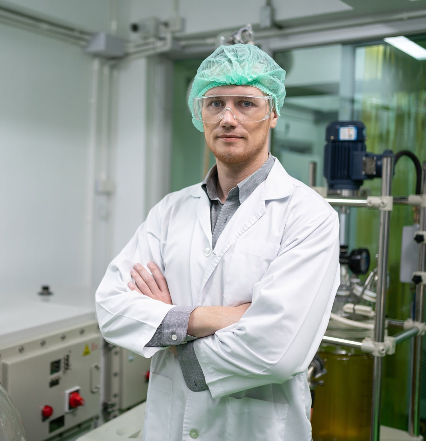 Medical professional in a lab coat standing inside a lab in front of medical equipment with his arms crossed.