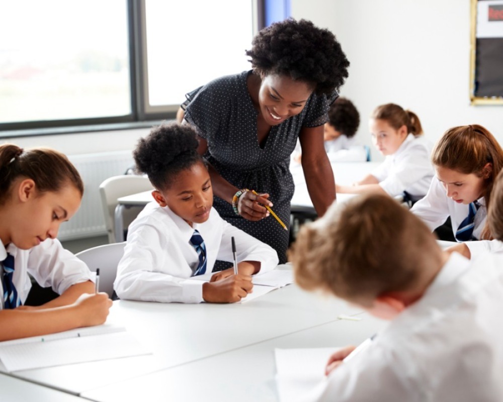 primary children with a teacher leaning over in class