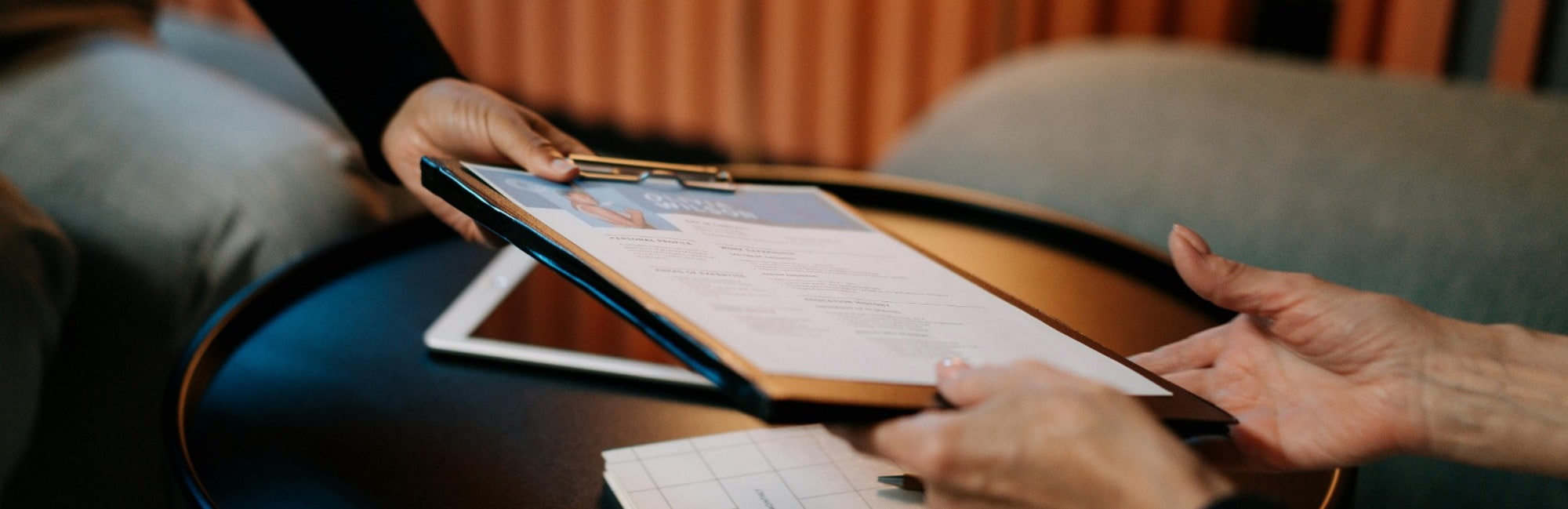 A woman holds a clipboard with her Transactional Finance CV on it while a man reviews the CV.