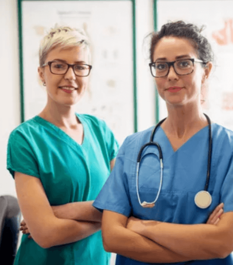 Two female nurses standing up with the arms crossed, smiling.