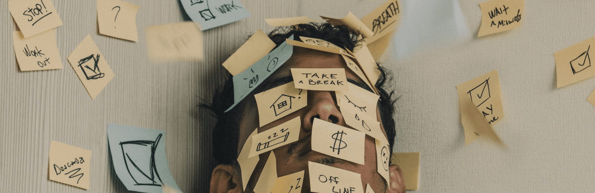 A man with his head covered in sticky notes, visually representing the stress of too many responsibilities.